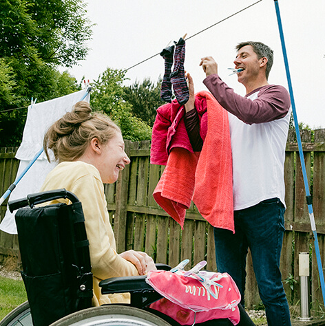 Father hanging clothes on the line with his daughter in her wheelchair.