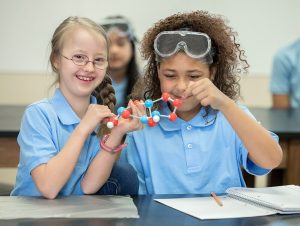 Two young female students with Down syndrome holding a science model.