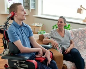 Teenage boy in a wheelchair talking to his mother at home.