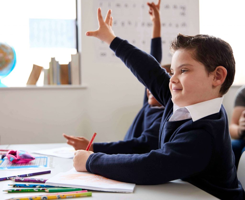 Young boy with Down syndrome raising his hand in class.