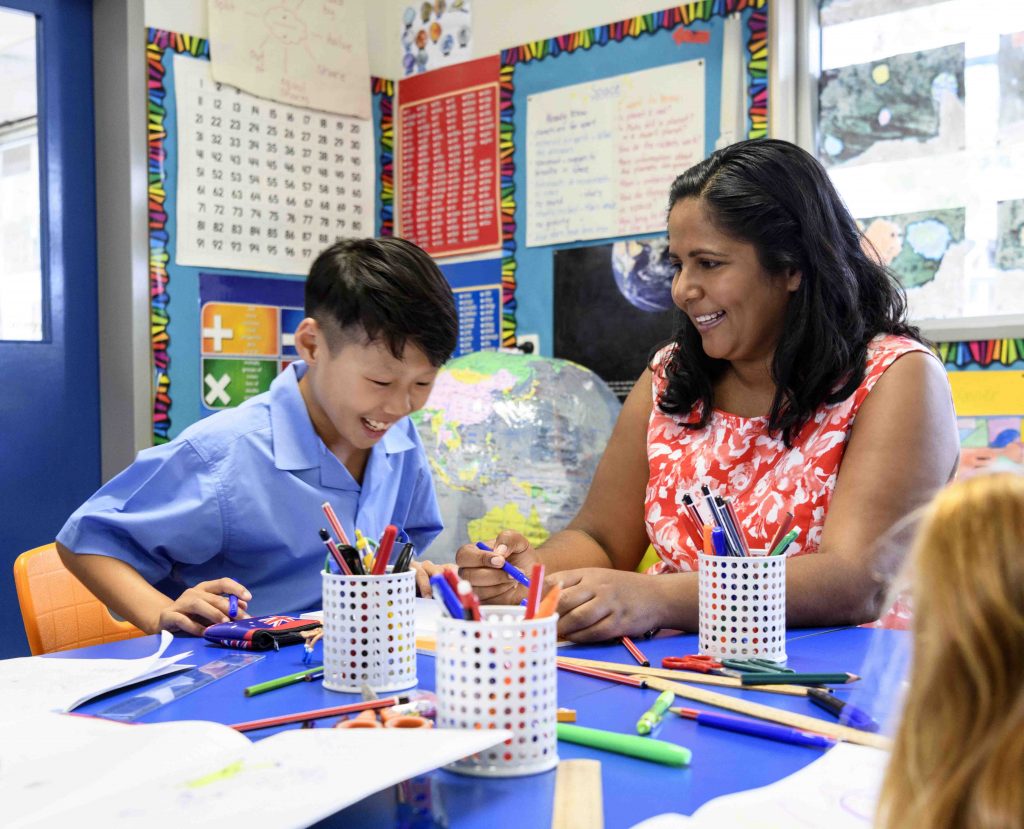 Female teacher working with a young male student at a table in the classroom.