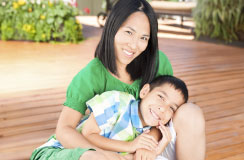 Mother and primary-aged son sit on the de. The son is snuggled on his mother's lap.