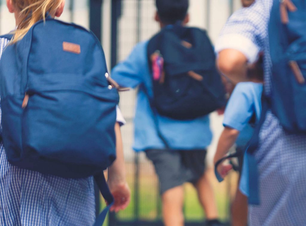 School children wearing backpacks walking into school.