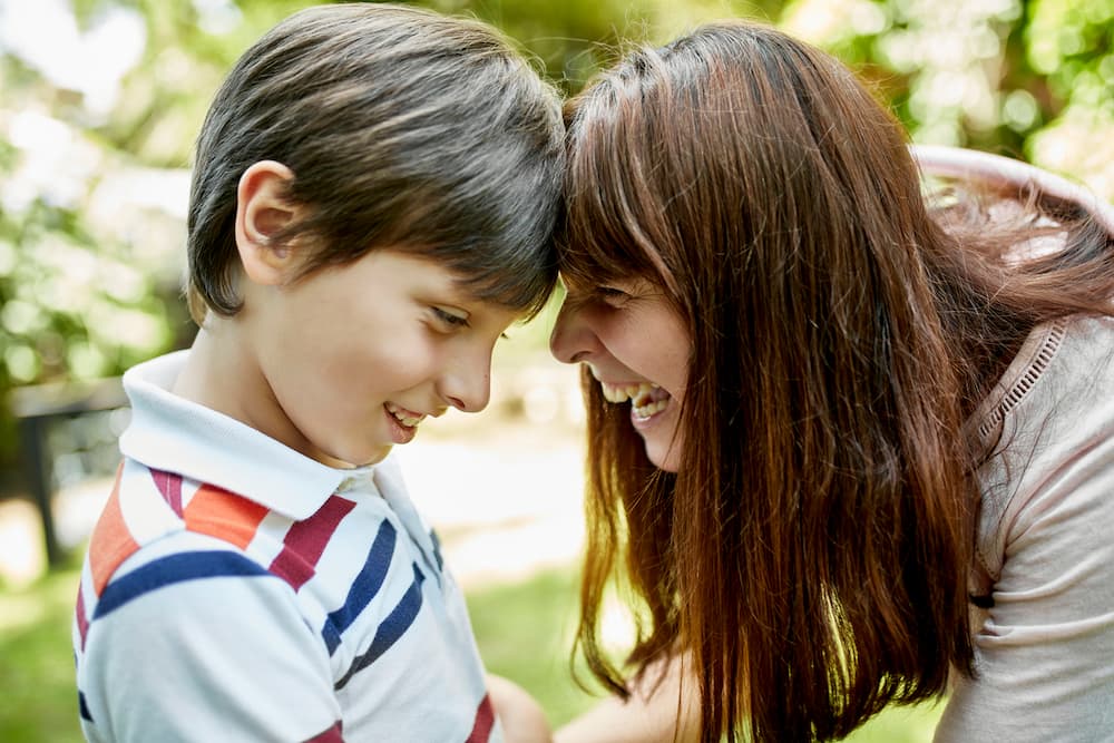 A young schoolboy with his mother. They are both smiling.