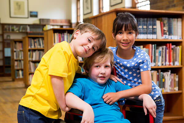 Young boy in a wheelchair with two friends who have their arms around him in the library.