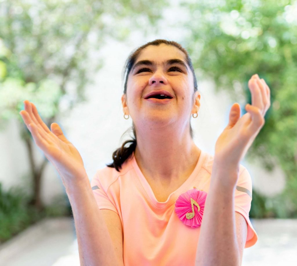 A teenage girl with disability singing and clapping outside.