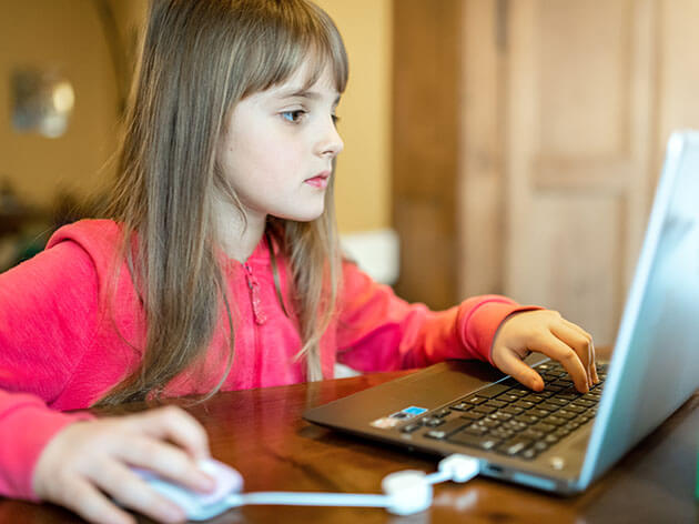 Eight year old girl learning from home using a laptop computer with a mouse.