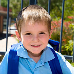 A young school boy wearing his back back standing in the school yard.