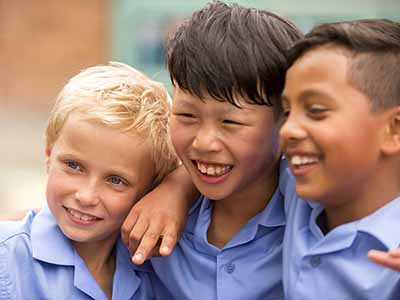 Three boys laughing together having fun in the playground at primary school.