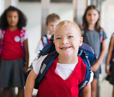 Smiling boy with Down syndrome leading a group of students walking down the corridor at school.