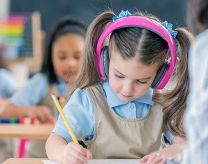 تلميذة صغيرة ترتدي سماعات الرأس أثناء الكتابة على مكتبها في المدرسة.