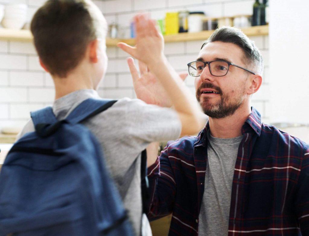 A dad giving his son a high five before he goes off to school.