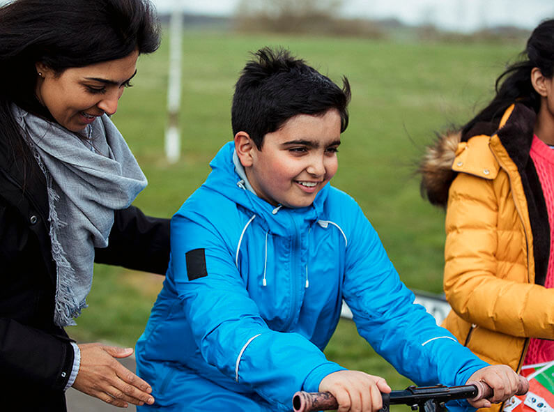 A mother supports her son to ride a scooter.
