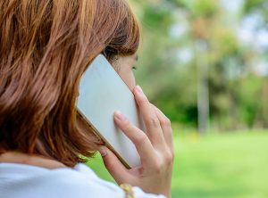 امرأة تتحدث على الهاتف المحمول ، تقف في الخارج تنظر إلى المسافة ، فقط جانب وجهها وشعرها في الأفق.