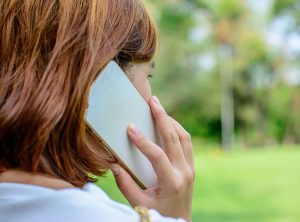 A woman talking on mobile phone, she is standing outside looking into the distance, only the side of her face and hair is in view.