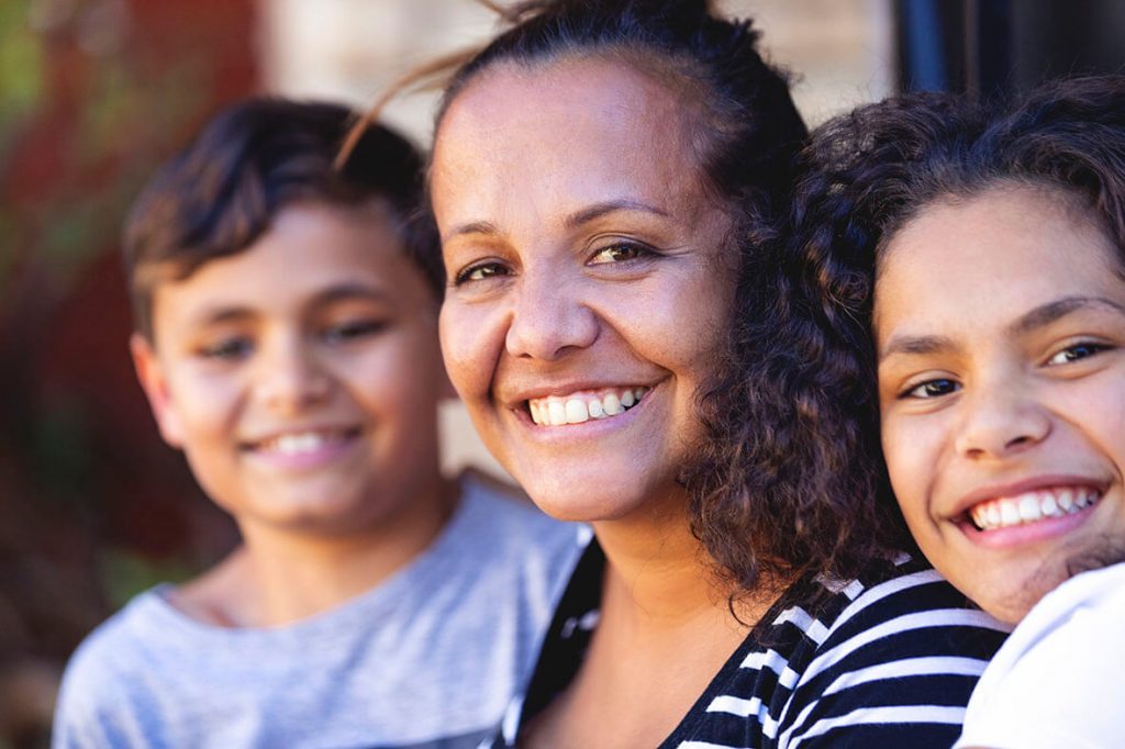 A smiling mum and her two children on either side sitting on the front porch.