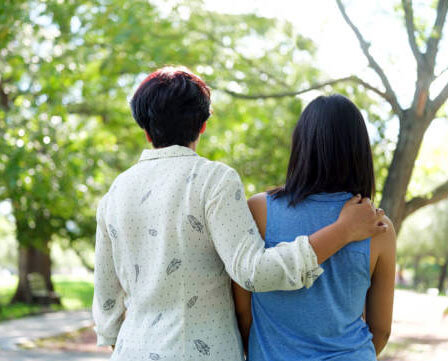 Back view of mother and daughter standing together outside in a park.