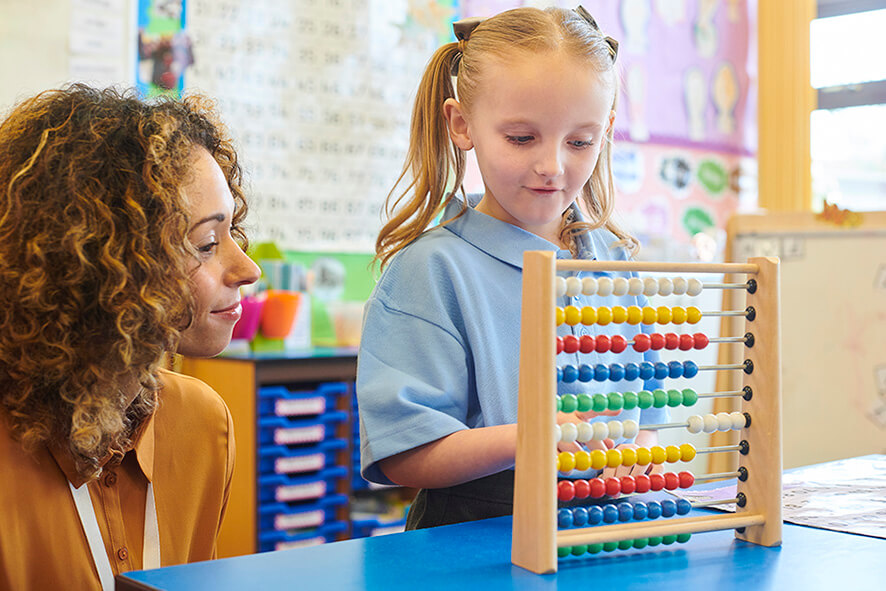 A young female student moves beads on an abacus as her female teacher watches on.
