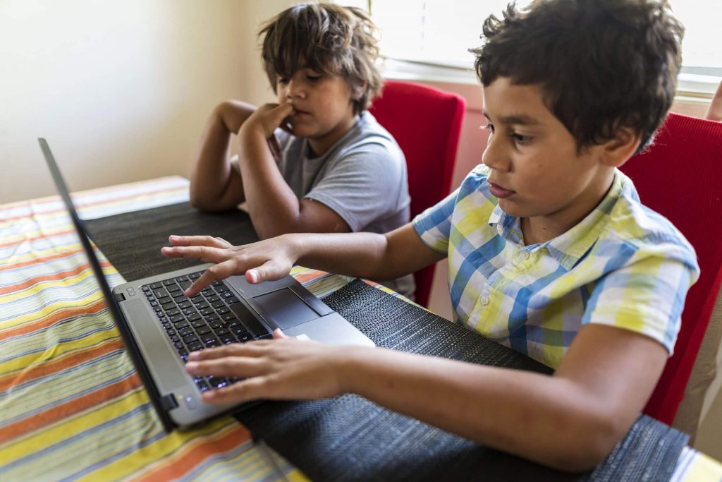 दो आदिवासी लड़के घर पर लैपटॉप का उपयोग करते हैं।