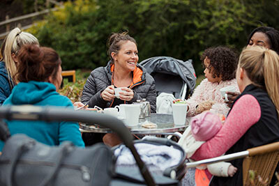 A group of mums sitting at a table in the park having a coffee and a chat.