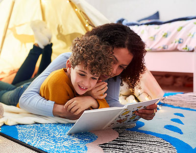 Mother reading with son on the floor in a tent in the bedroom.