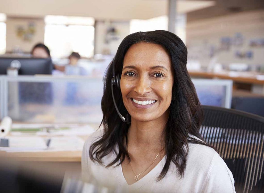 Smiling woman wearing a headset working at her desk in the office.