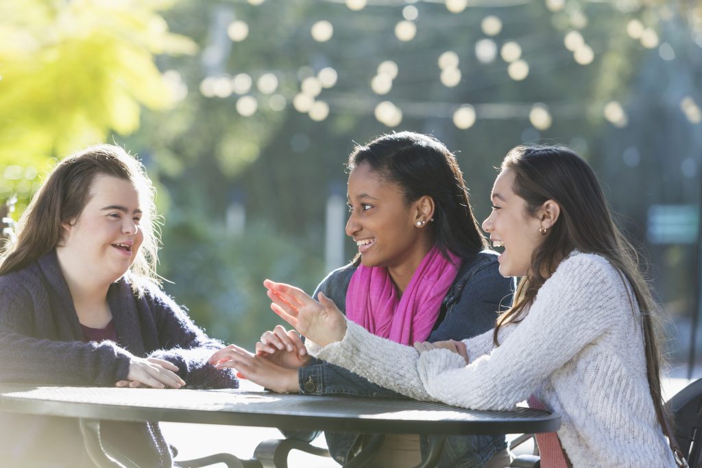Three teenage girls sit at a park table smiling.
