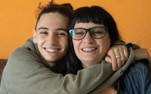 Teenager hugging his Mum. They are sitting on the couch and smiling.