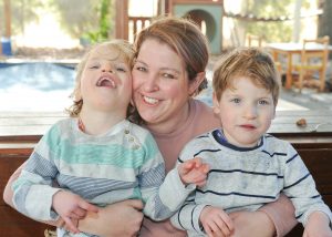 Mum is sitting with her two children at the park. Both have cerebral palsy and are sitting on her knee.