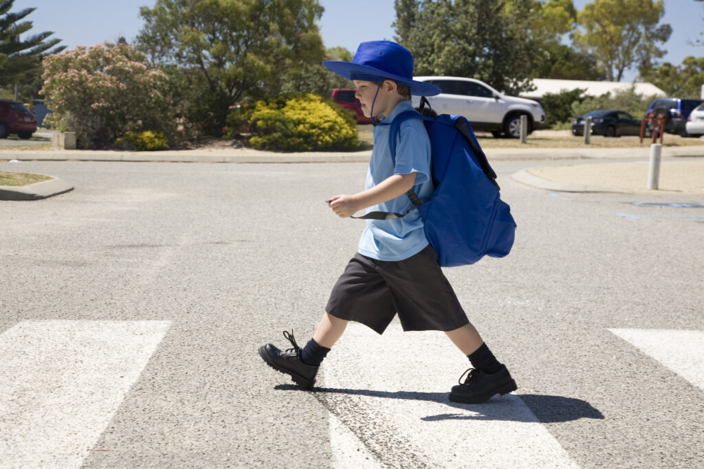 Young primary school boy in uniform walking across the school crossing and wearing a school bag.