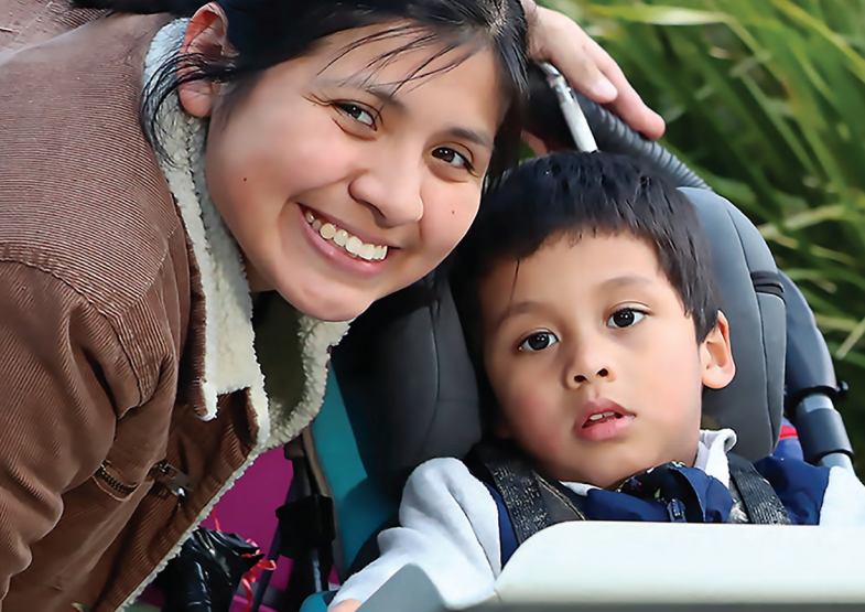 Một người mẹ và đứa con trai mới biết đi của họ. Con trai đang ở trong xe đẩy, và người mẹ đang mỉm cười.