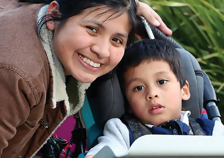 A mother and their toddler son. The son is in a stroller, and the mother is smiling.