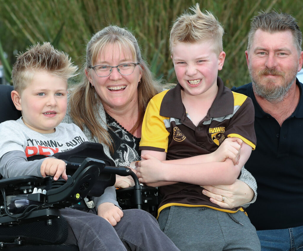 A family with two boys, a mother, and father. One boy is sitting in a wheelchair, the other is sitting on the mother's lap.