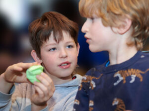 A boy showing another child a green toy in his hand.
