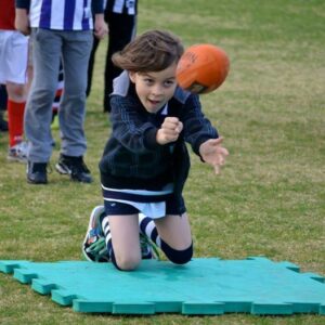 A boy taking part in Auskick. He is handballing a ball.