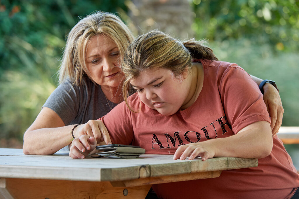 A mother and daughter sitting at a table looking at a phone together.