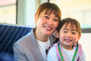 A young girl rides the bus with her mum. She is wearing a hidden disabilities sunflower lanyard.