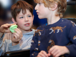 A boy showing another child a green toy in his hand.