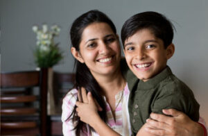 A mother is smiling while sitting with her son in the lounge room.