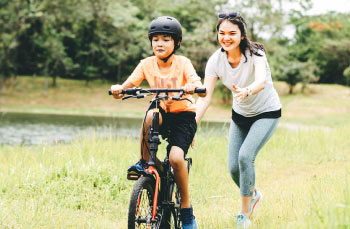 A young boy learning to ride a bike with his mother.
