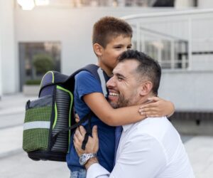 A school boy wearing a backpack hugging his father.