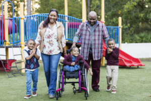 Một gia đình đa dạng về văn hóa tại một sân chơi. Có một người mẹ, người cha, hai bé trai sinh đôi và một bé gái ngồi xe lăn.