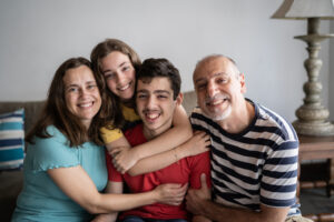 Portrait of a family at home. A mum, dad brother and sister sit on the couch, smiling.