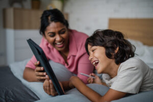 A mother and son laugh together at something on a digital tablet.